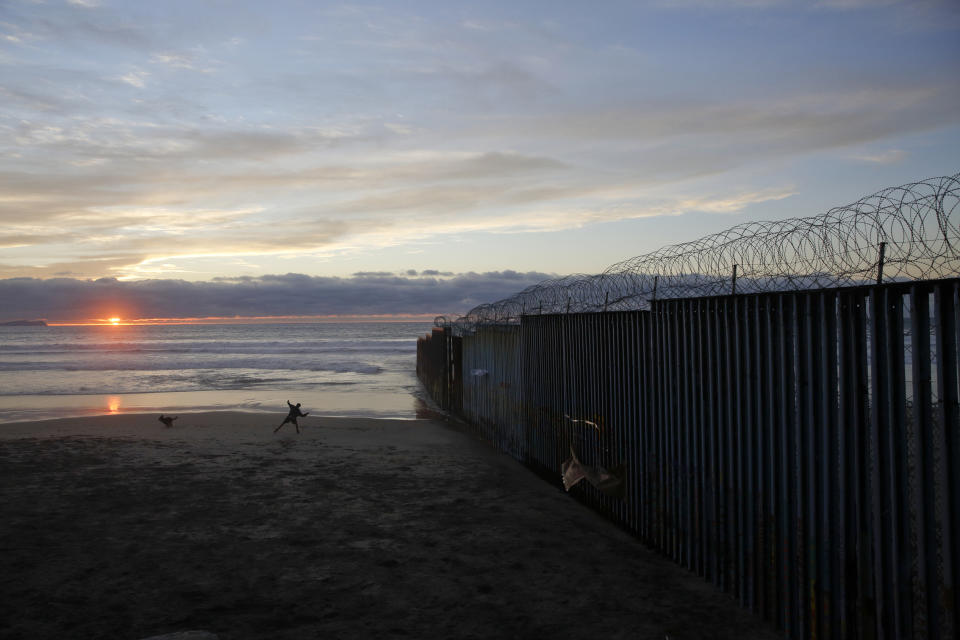 FILE - In this Jan. 9, 2019, file photo, a man throws a ball for his dog next to the border wall topped with razor wire in Tijuana, Mexico. In his demands that Congress set aside $5.7 billion for a border wall, President Donald Trump insists a physical barrier would stop heroin entering the U.S. from Mexico. But U.S. statistics, analysts and testimony at the trial of drug kingpin Joaquin "El Chapo" Guzman in New York show that most hard drugs entering the U.S. from Mexico come through land ports of entry staffed by agents, not open sections of the border. (AP Photo/Gregory Bull, File)