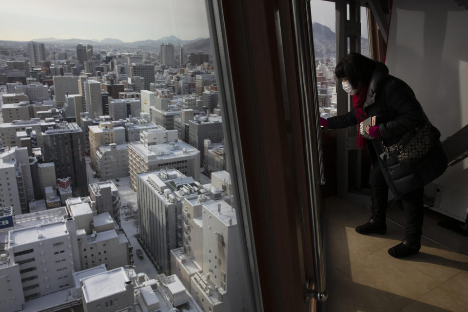 In this Feb. 6, 2020, photo, a tourist wearing a mask views snow-covered buildings from the Sapporo TV Tower's observation deck in Sapporo, Hokkaido, Japan. The Japanese island of Hokkaido is declaring a state of emergency over the rapid spread of the new virus there. (AP Photo/Jae C. Hong)