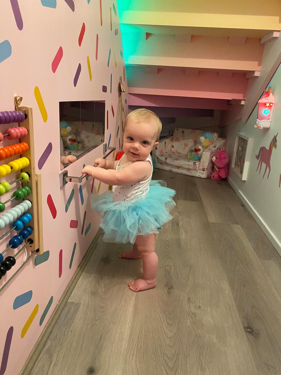 baby girl in tutu poses in under stair colourful rainbow playroom