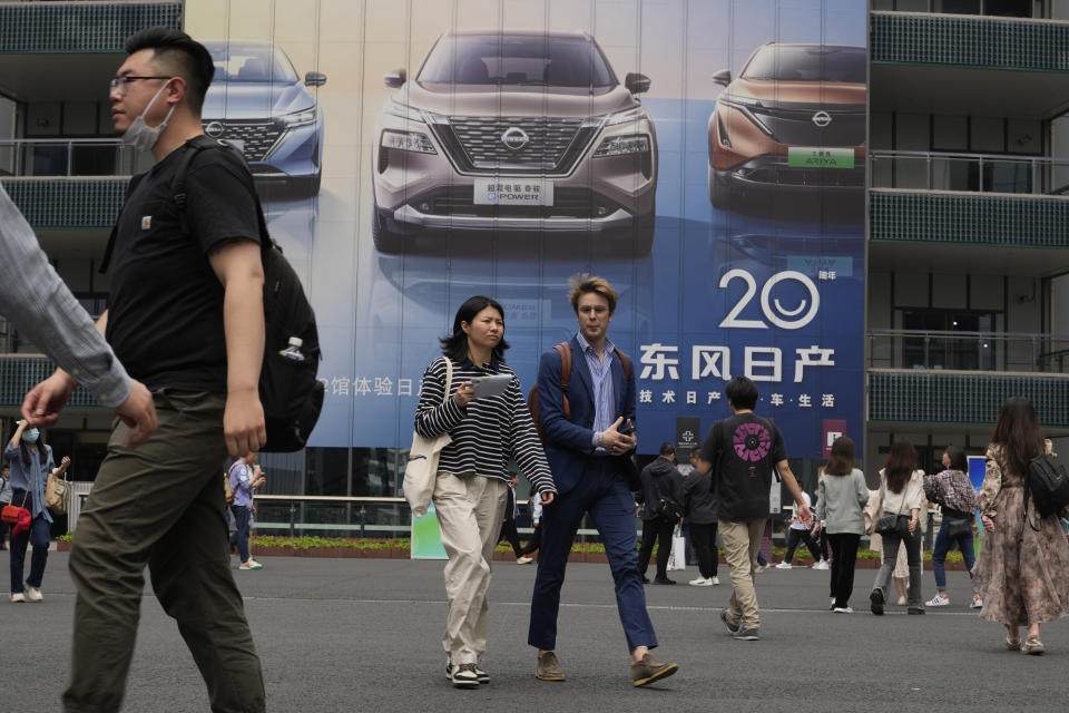 Attendees pass by an advertisement for Nissan cars during the Auto Shanghai 2023 show in Shanghai, Tuesday, April 18, 2023. Global and Chinese automakers plan to unveil more than a dozen new electric SUVs, sedans and muscle cars this week at the Shanghai auto show, their first full-scale sales event in four years in a market that has become a workshop for developing electrics, self-driving cars and other technology. (AP Photo/Ng Han Guan)