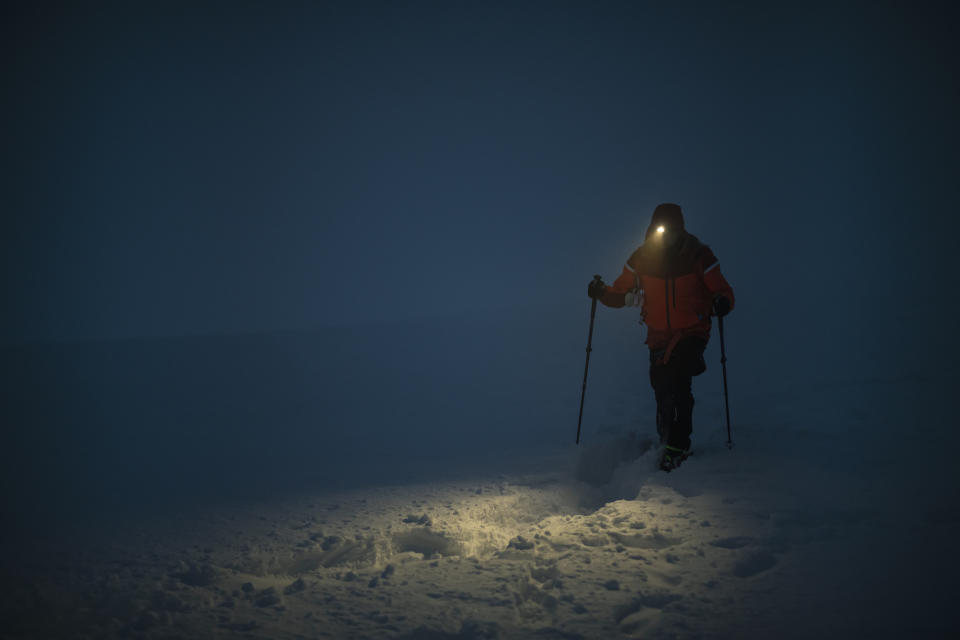 Person walking in the snow using ski poles at night, with a headlamp illuminating their path