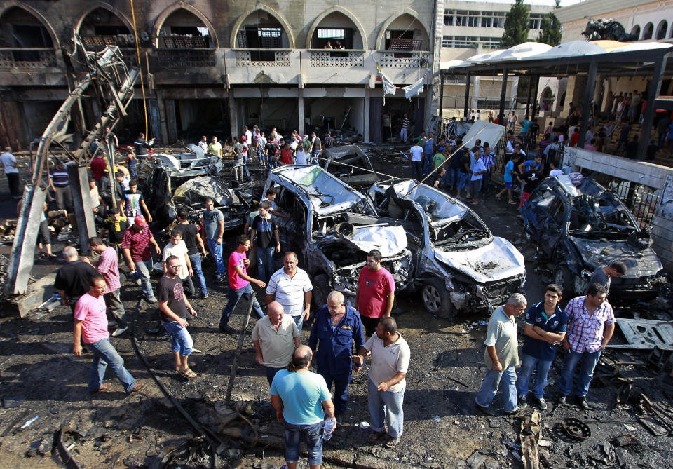 FILE - In this Friday, Aug. 23, 2013 file photo, people gather outside the al-Taqwa mosque amid charred cars and wide damage at the site of a car bombing, which killed dozens, in the northern city of Tripoli, Lebanon. A Lebanese court has sentenced Friday, Nov. 1, 2019 a man to death in a 2013 twin car bombs in the northern city of Tripoli that killed 47 people. (AP Photo/Bilal Hussein, File)