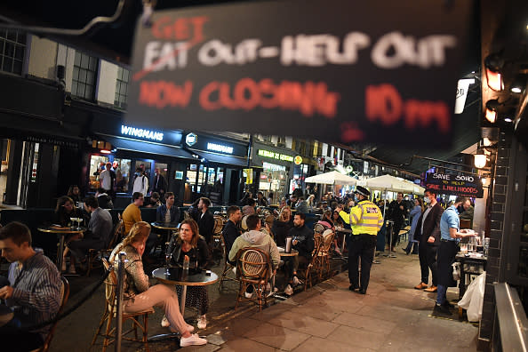 A sign reading 'Get out - Help out' hangs from a pub in Soho as a Police officer speaks to drinkers  in London, England. 