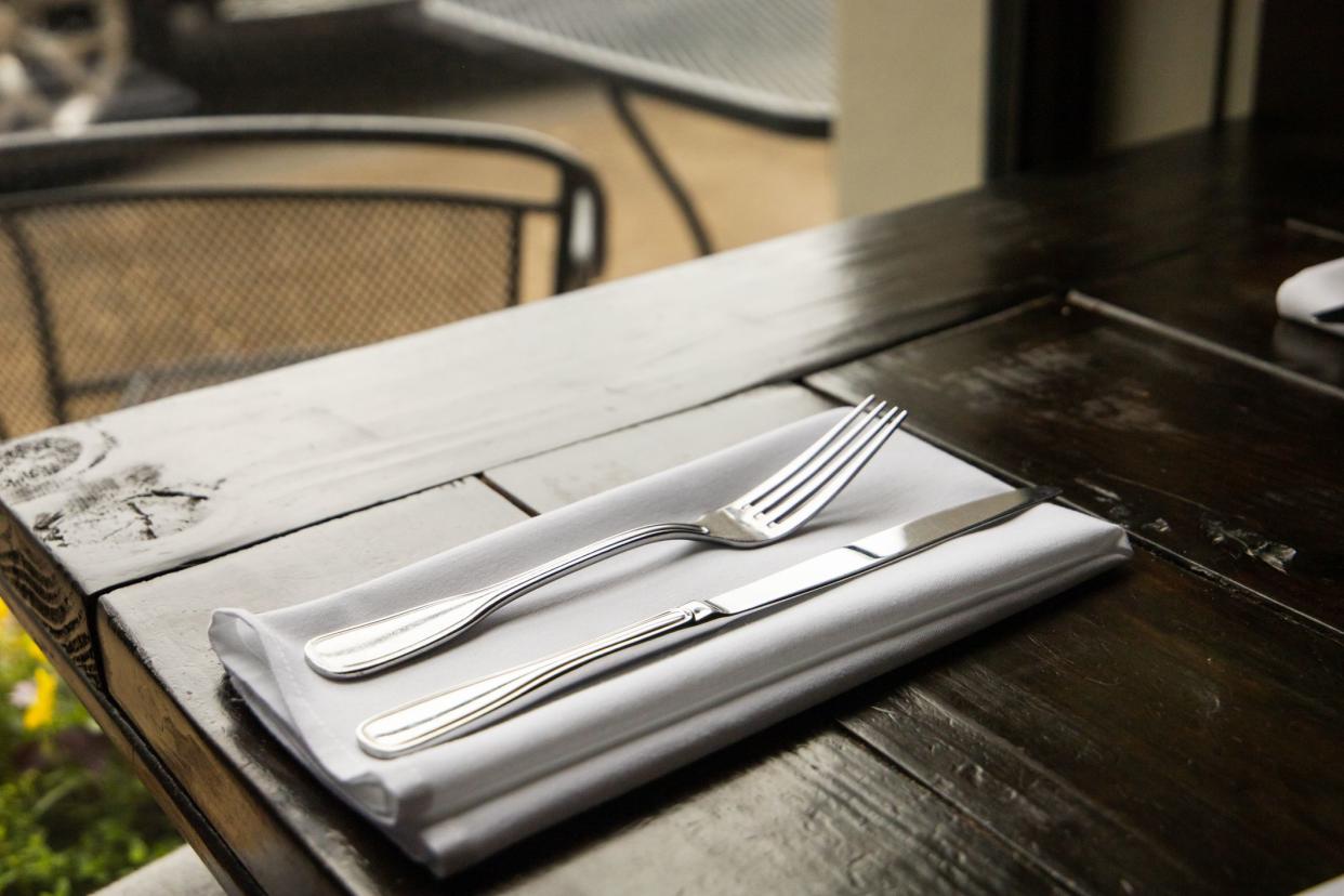 A silverware setting of a fork and knife on a wood table at a high-end restaurant near a window. The table is placed and ready for dinner and service.