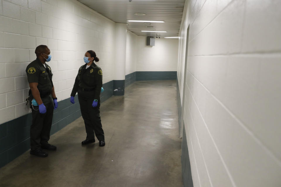 In this April 16, 2020, photo Christopher Lumpkin, left, and Sonia Munoz, custody assistants, talk in the hallway of the hospital ward at the Twin Towers jail in Los Angeles. Across the country first responders who've fallen ill from COVID-19, recovered have begun the harrowing experience of returning to jobs that put them back on the front lines of America's fight against the novel coronavirus. (AP Photo/Chris Carlson)