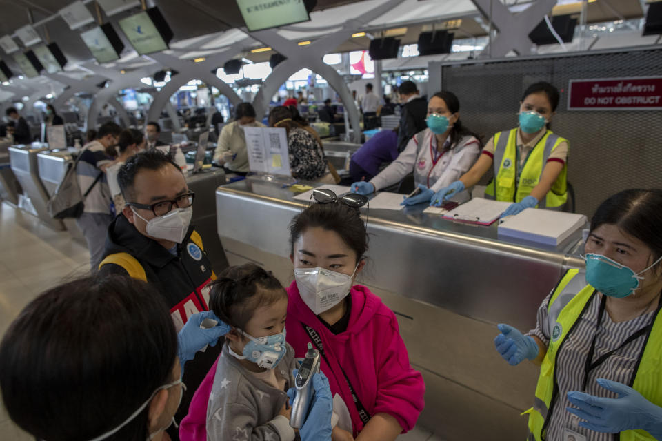 A health worker reaches to check the temperature of a tourist from Wuhan, China, as they line for a charter flight back to Wuhan at the Suvarnabhumi airport, Bangkok, Thailand, Friday, Jan. 31, 2020. A group of Chinese tourists who have been trapped in Thailand since Wuhan was locked down due to an outbreak of new virus returned to China on Friday. (AP Photo/Gemunu Amarasinghe)
