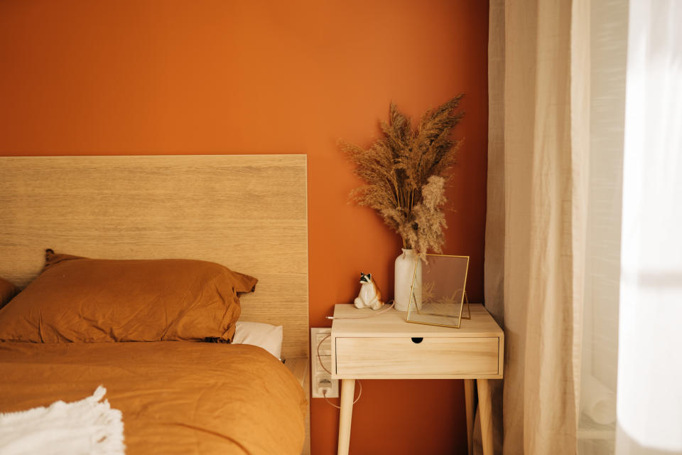 Close-up on simple, white bedside table with decorations next to comfortable bed in bedroom with dark blue wall