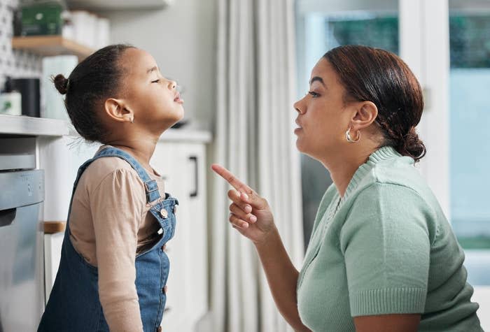 Woman in a green top talking to a child who is making a face, in a kitchen setting