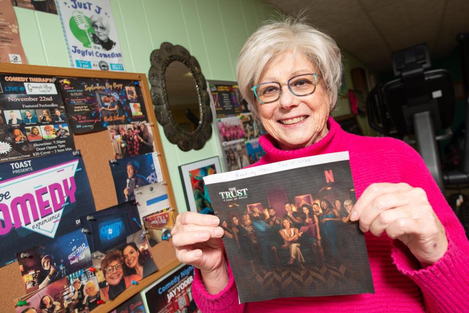 Jay Patterson displays a promotional photo from her upcoming Netflix show "The Trust: A Game of Greed." A collection of Patterson's comedy and life achievements can be seen Thursday on a wall in her basement.