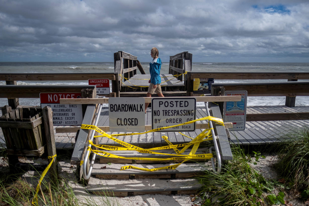 Someone walks blithely along a boardwalk fenced off by tangles of yellow tape and two signs saying Boardwalk Closed and Posted No Trespassing by Order.