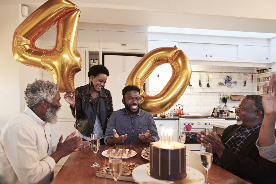 smiling woman holding number 40 helium balloons while standing by man during birthday party with family at home