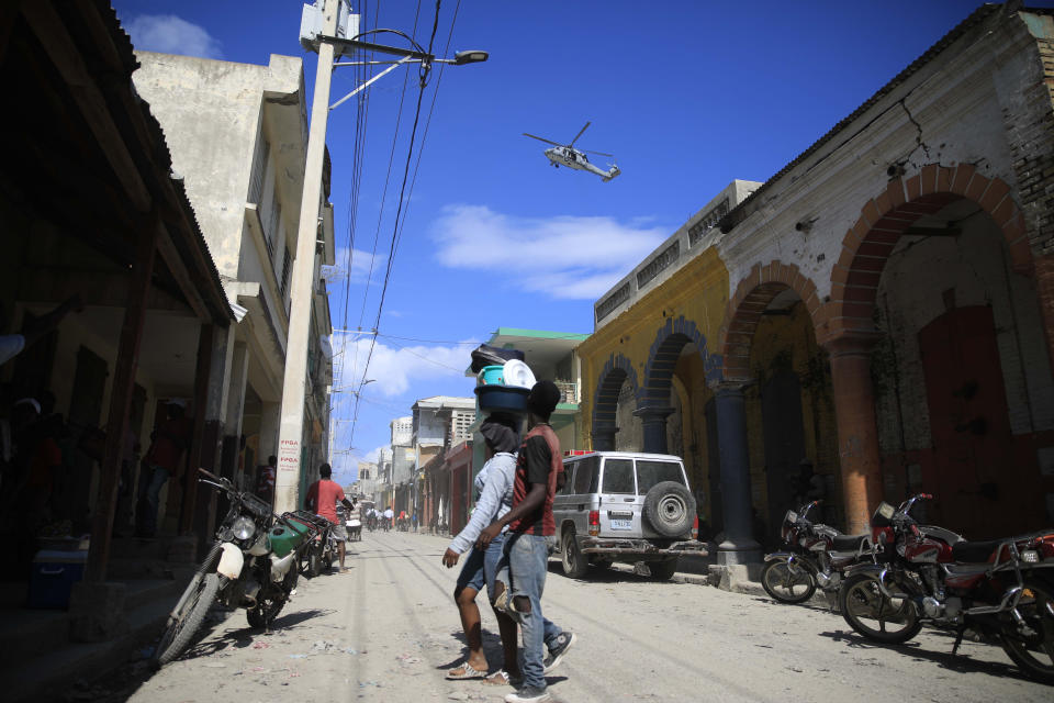 A USN helicopter flies overhead during a protest against the arrival of the USNS Comfort hospital ship in Jeremie, Haiti, Tuesday, Dec. 13, 2022. The USNS Comfort is on a humanitarian mission to provide dental and medical services. (AP Photo/Odelyn Joseph)