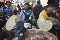 A devotee wearing a protective face mask amid the new coronavirus pandemic and carrying his Saint Jude statue, watches vendors prepare tacos during the annual pilgrimage honoring Jude, the patron saint of lost causes, in Mexico City, Wednesday, Oct. 28, 2020. Thousands of Mexicans did not miss this year to mark St. Jude's feast day, but the pandemic caused Masses to be canceled and the rivers of people of other years were replaced by orderly lines of masked worshipers waiting their turn for a blessing. (AP Photo/Marco Ugarte)