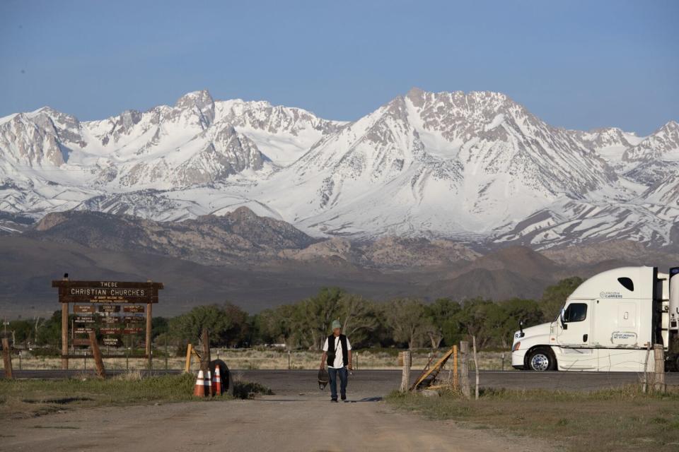 A fishermen walks against the backdrop of snow-covered mountains.