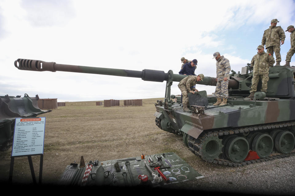 Half a dozen troops of the Turkish Armed Forces prepare an armored artillery vehicle on a flat plain. 