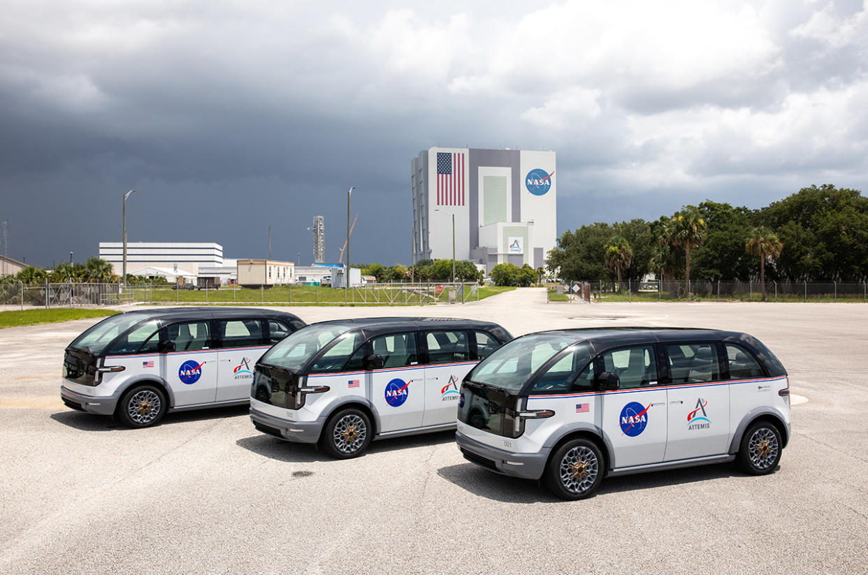  three electric minivans with nasa logos sit in a parking lot in front of a large building 