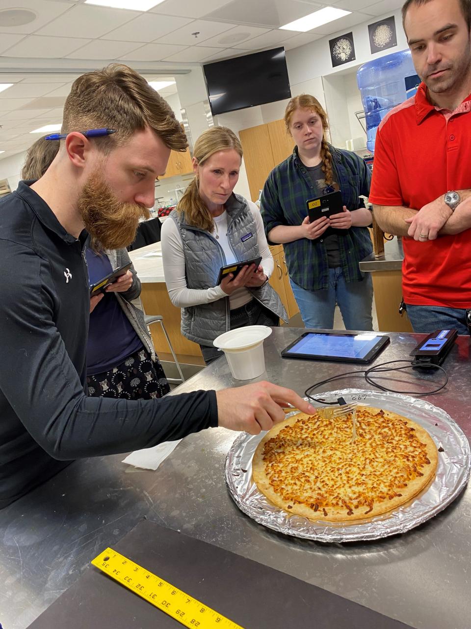 Sensory panelists, from left, Brian Hanson, Kelly Kluck and Carolyn Haswell along with Brandon Prochaska, program coordinator (in red) scrutinize the "stretch characteristics" of mozzarella pizza cheese during a testing session held March 6, 2024, at the Center for Dairy Research of the University of Wisconsin-Madison.