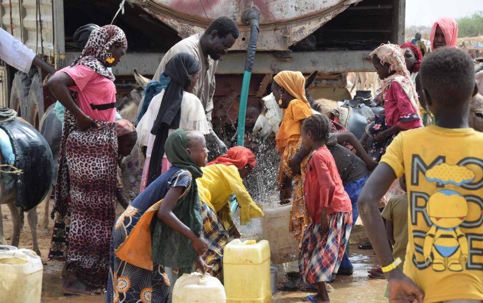 Refugees fill containers and drink from a water tank in Koufroun, Chad, near Echbara - GUEIPEUR DENIS SASSOU/AFP