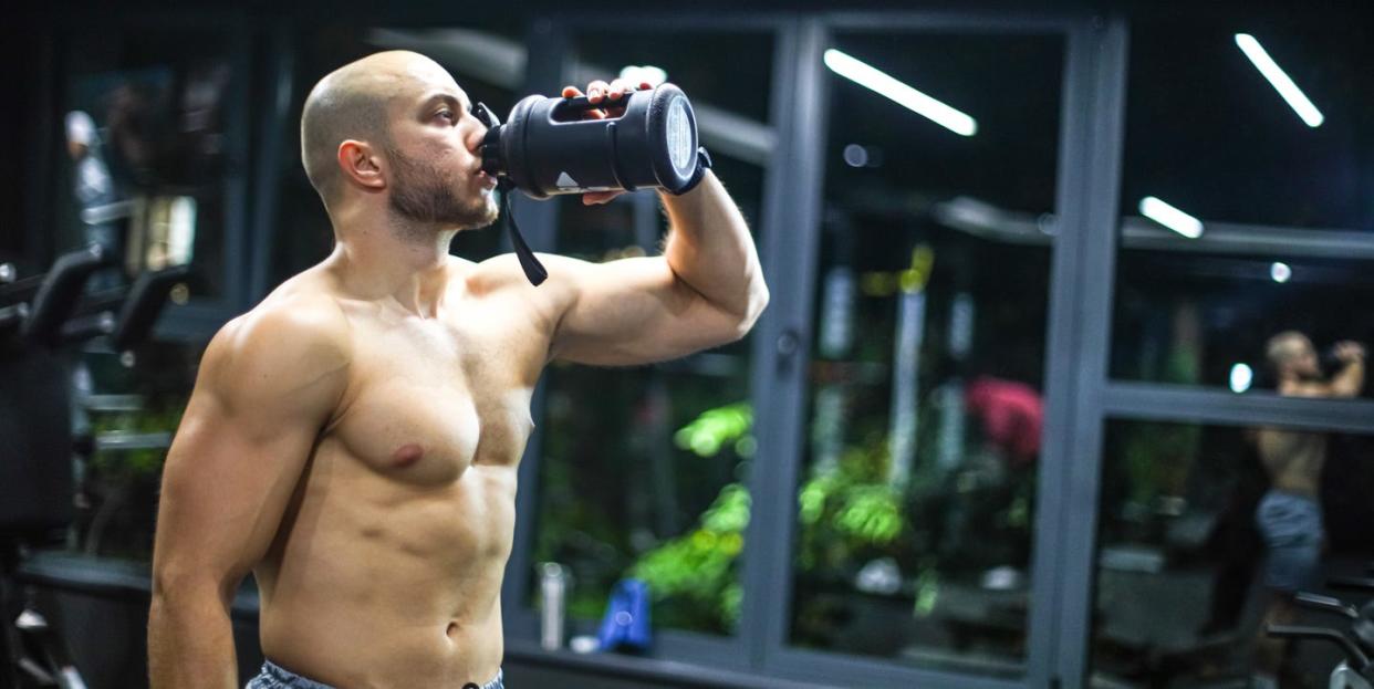 muscular men drink his nutritional supplement in gym