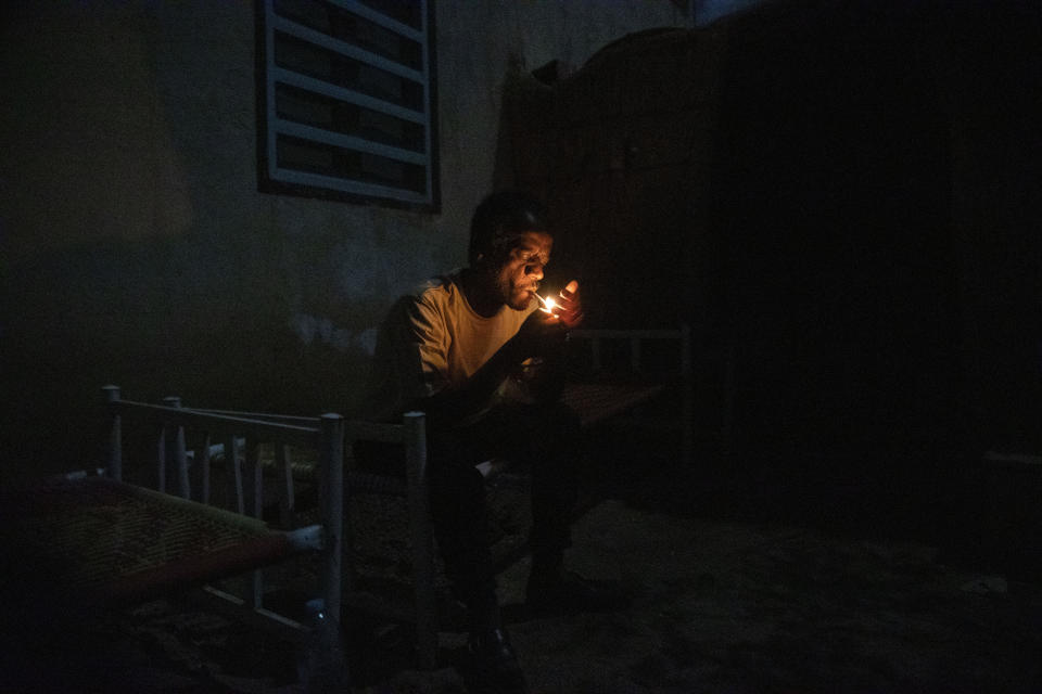 Surgeon and doctor-turned-refugee, Dr. Tewodros Tefera, lights a cigarette and rests on his bed after finishing his work, at the Sudanese Red Crescent clinic in Hamdayet, eastern Sudan, near the border with Ethiopia, on March 22, 2021. (AP Photo/Nariman El-Mofty)