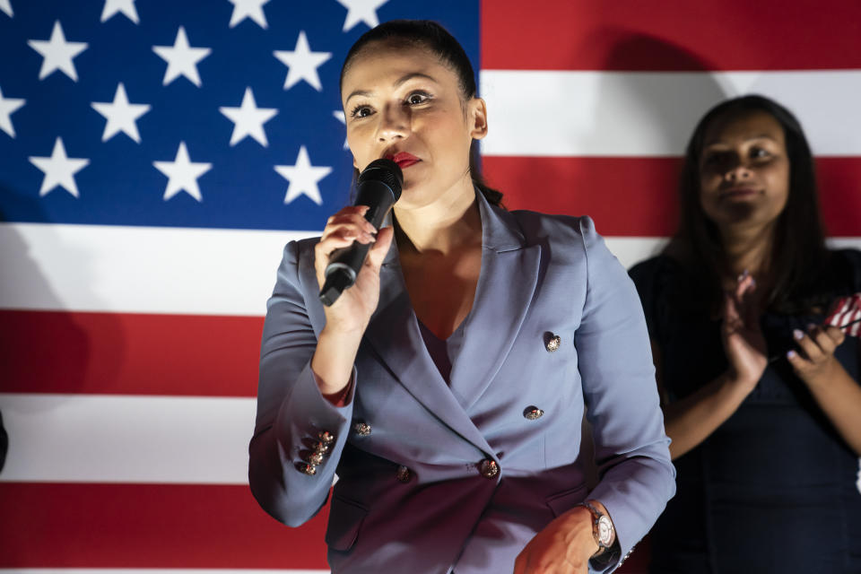 Yesli Vega holding a microphone standing in front of the American flag.
