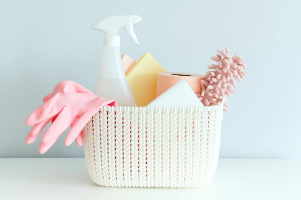 A set of tools for cleaning the room in a plastic basket on the shelf on a blue wall background