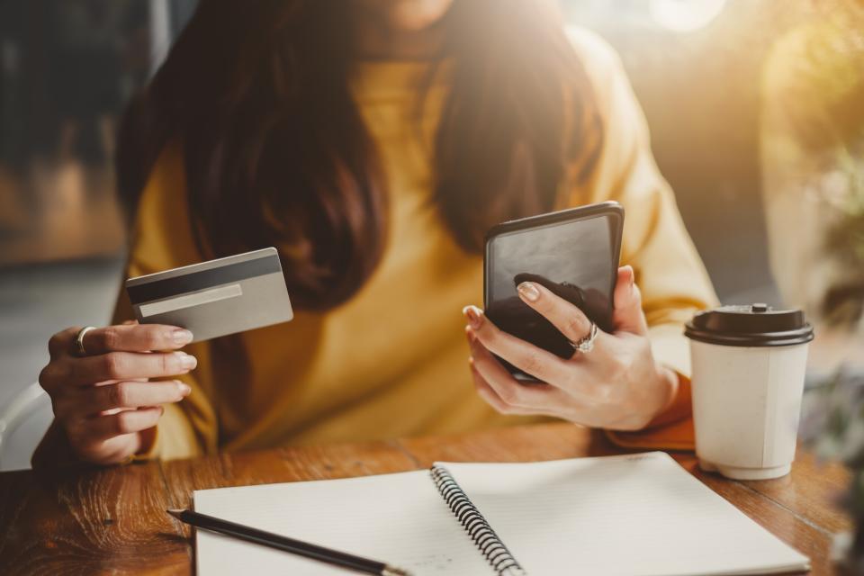 Woman sitting at a table with a credit card, notebook, phone, and coffee