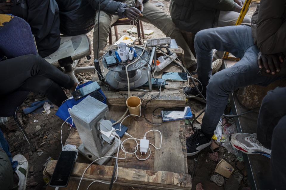 A group of migrants charge their phones at an abandoned warehouse turned migrant camp in Calais, northern France, on Wednesday, May 15, 2024. (AP Photo/Bernat Armangue)