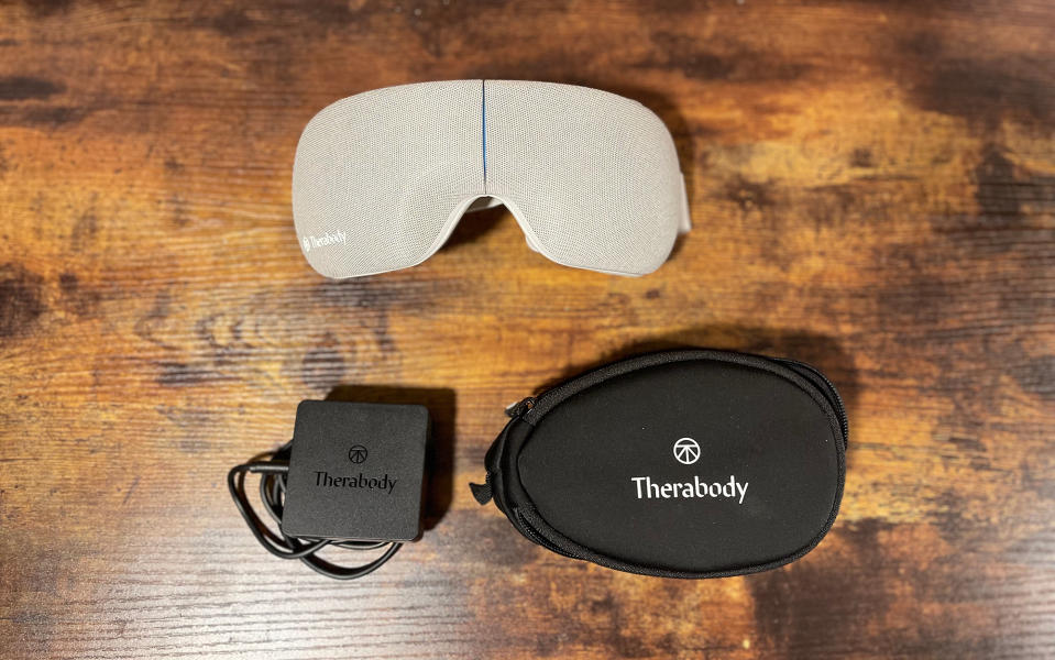 An original photo from a SPY editor of Therabody Smartgoggles next to their case and charger on a wooden desk