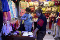 FILE - In this Nov. 4, 2017, file photo, an Uyghur woman teaches a child the Chinese language from a textbook at a shop along an underpass in Kashgar in western China's Xinjiang region. A human rights group appealed to the United Nations on Monday, April 19, 2021 to investigate allegations China's government is committing crimes against humanity in the Xinjiang region. (AP Photo/Ng Han Guan, File)