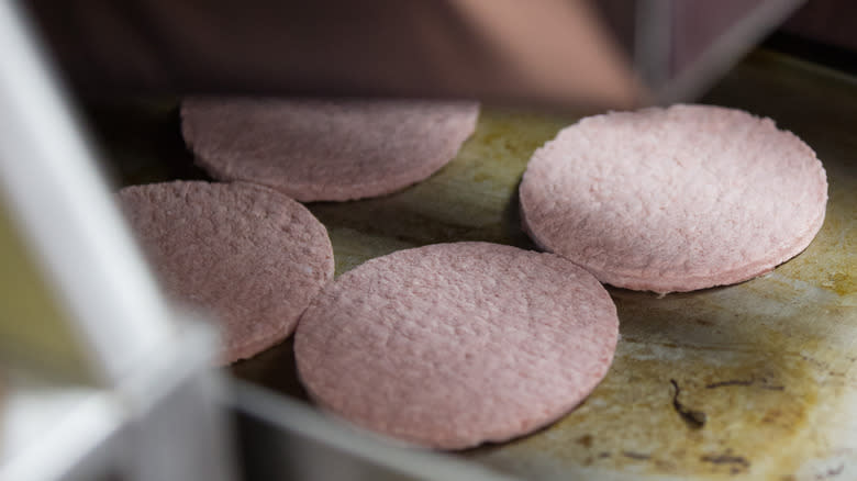 Four frozen burger patties on griddle