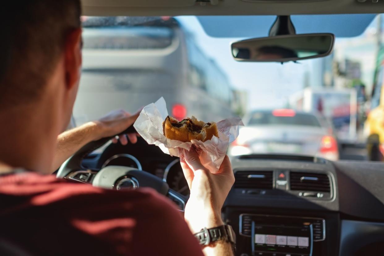 Man driving car while eating hamburger. Waiting and standing in traffic jam