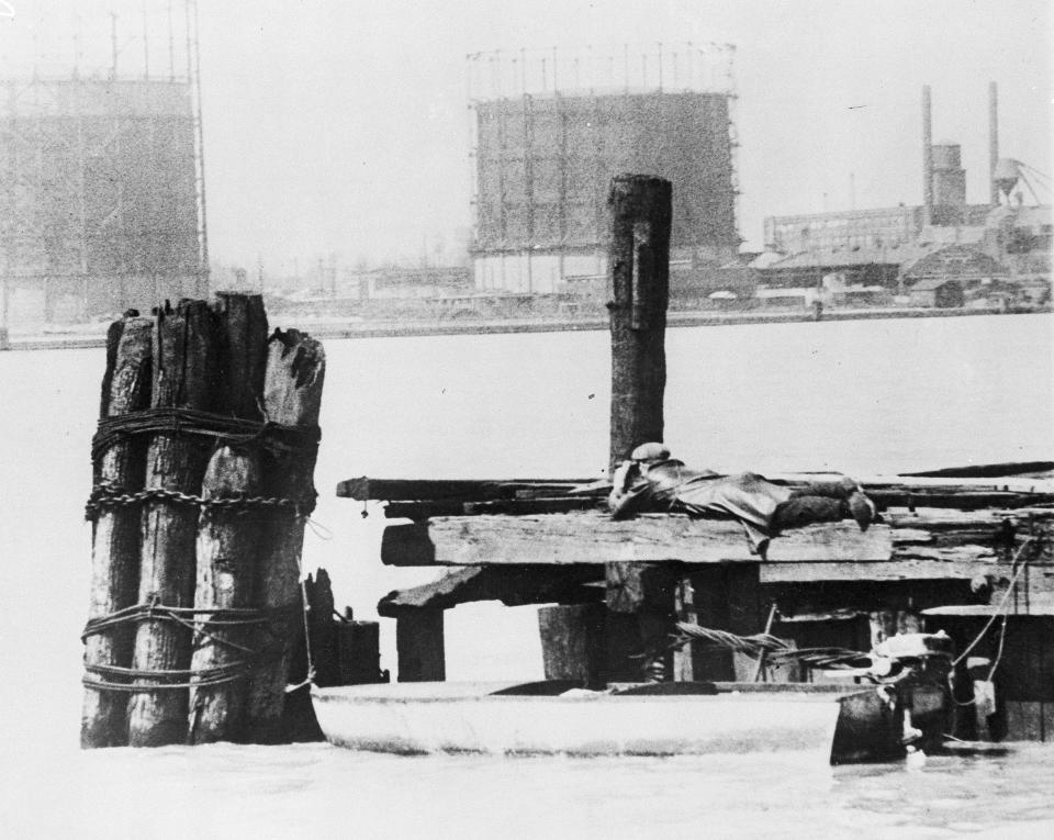 FILE - In this April 28, 1929, file photo a rum runner in Windsor, on the Canadian side of the Detroit River, watches with field glasses for lookout on the American side to signal that no prohibition agents are in sight. His outboard motorboat, loaded with illegal liquor, is shown beneath pilings. (AP Photo, File)