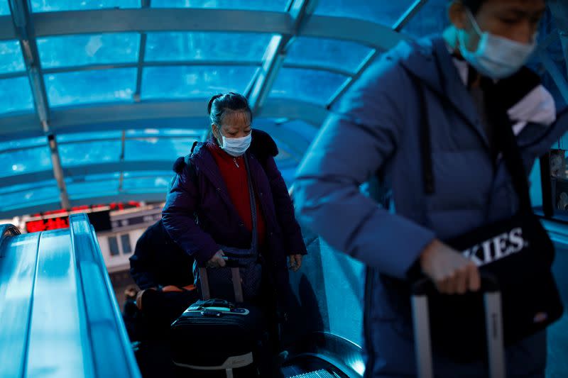 People wearing face masks carry their luggage as they use an escalator near Beijing Railway Station as the country is hit by an outbreak of the new coronavirus, in Beijing