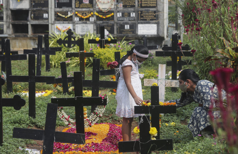 Relatives wearing face masks as a precaution against the coronavirus put flowers at the grave of a deceased relative during All Souls Day in Mumbai, India, Monday, Nov. 2, 2020. (AP Photo/Rafiq Maqbool)