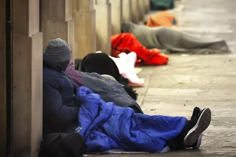 A man sits by a wall with a sleeping bag