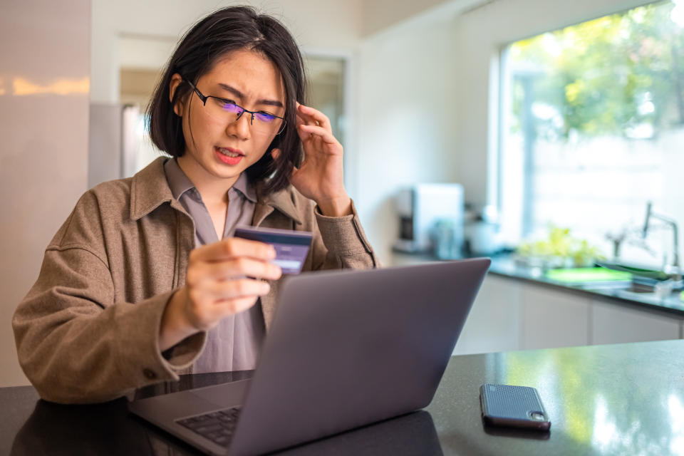 Young Asian woman holding a credit card and looking concerned with being involved in a scam, illustrating a story on Facebook Marketplace and Carousell rating lowest in Singapore.