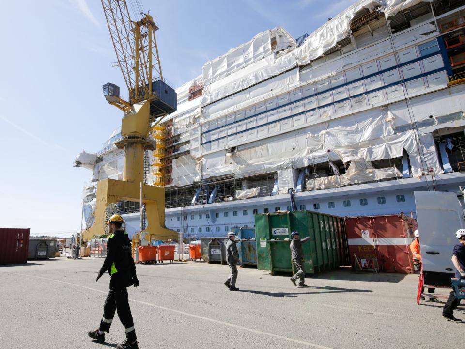 Workers at a port with a large yellow crane where the Icon of the Seas is being built.