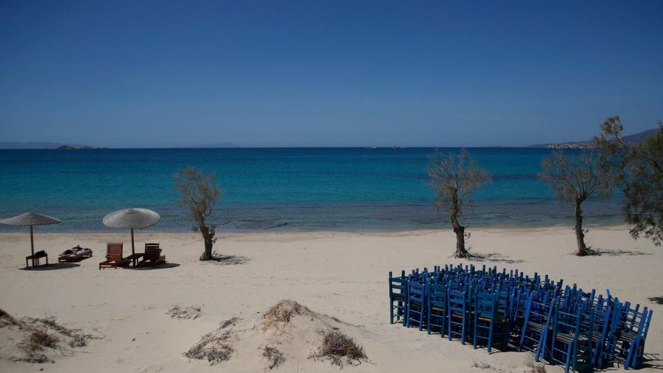 Ein Tourist genießt die Sonne, während Tavernenstühle am Strand von Plaka auf der Ägäisinsel Naxos gelagert werden.