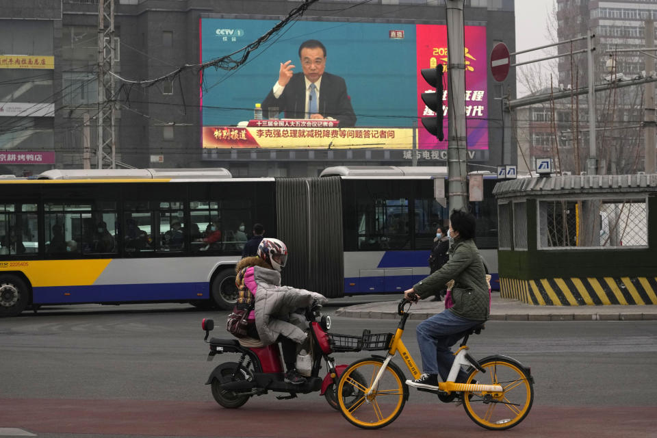 People ride past a large video screen at an intersection showing Chinese Premier Li Keqiang as he speaks during a press conference after the closing session of China's National People's Congress (NPC) in Beijing, Friday, March 11, 2022. (AP Photo/Ng Han Guan)