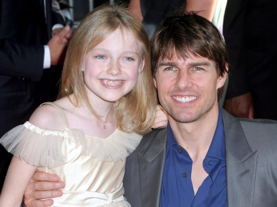 Dakota Fanning in a white dress next to Tom Cruise in a grey jacket and blue shirt