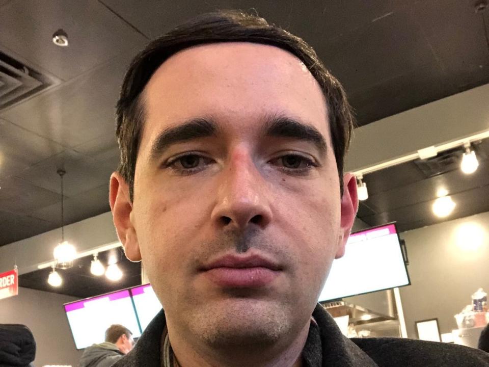 Business Insider reporter Alex Bitter faces the camera and wears a black coat and multicolor winter scarf while in a poke restaurant