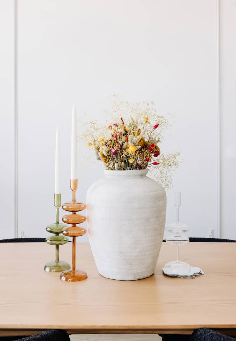 Dining table with large vase with dried flowers, and colored glass candlesticks with tapered candles