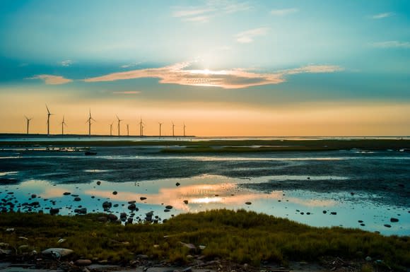 Wind turbines at sunset by the shore.