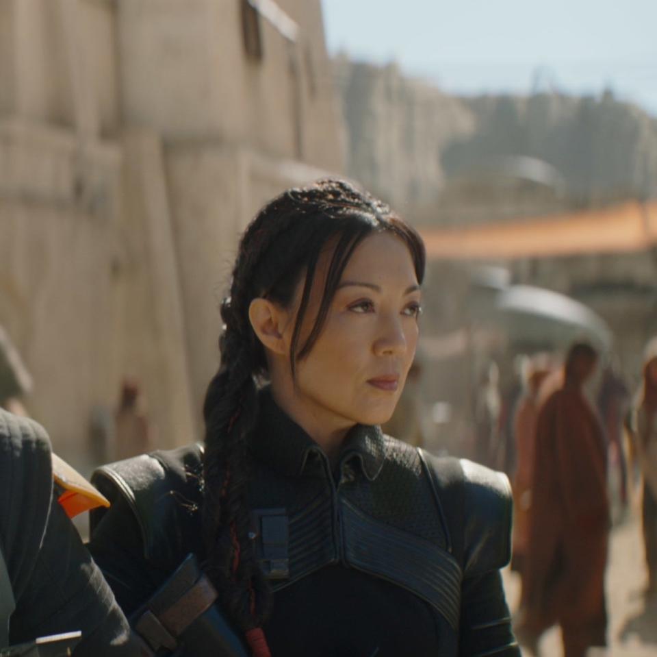 Temuera Morrison as Boba Fett and Ming-Na Wen as Fennec Shand in combat gear, standing in what appears to be a bustling desert town