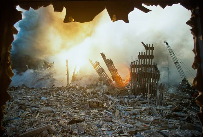 View from inside a damaged building looking out at the debris and wreckage of the World Trade Center after the 9/11 attacks, with smoke and sunlight visible