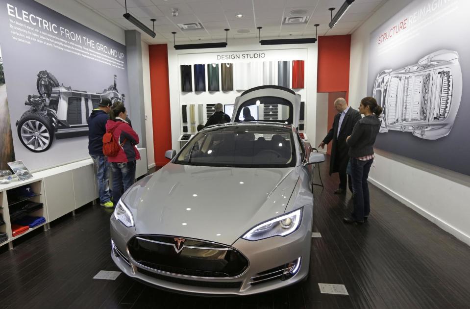 Customers check out a new Tesla all electric car, Monday, March 17, 2014, at a Tesla showroom inside the Kenwood Towne Centre in Cincinnati. Ohio auto dealers are sparring at the Statehouse with the California-based Tesla, which is selling it's next generation electric cars from three Ohio storefronts. Lawmakers in Ohio and other states are trying to block Tesla direct sales on grounds they undercut traditional auto dealerships. (AP Photo/Al Behrman)