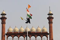 A Sikh man hangs on to a pole holding a Sikh religious flag along with a farm union flag at the historic Red Fort monument in New Delhi, India, Tuesday, Jan. 26, 2021. Tens of thousands of protesting farmers drove long lines of tractors into India's capital on Tuesday, breaking through police barricades, defying tear gas and storming the historic Red Fort as the nation celebrated Republic Day. (AP Photo/Supreet Sapkal)