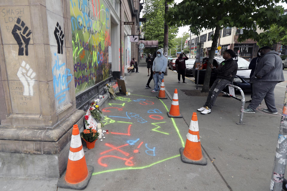 Friends and family stand near a growing memorial to a person named Lorenzo, Saturday, June 20, 2020, at the intersection of 10th Ave. and Pine St. near the Capitol Hill Occupied Protest zone in Seattle. A pre-dawn shooting near the area left one person dead and critically injured another person, authorities said Saturday. The area has been occupied by protesters after Seattle Police pulled back from several blocks of the city's Capitol Hill neighborhood near the Police Department's East Precinct building. (AP Photo/Ted S. Warren)