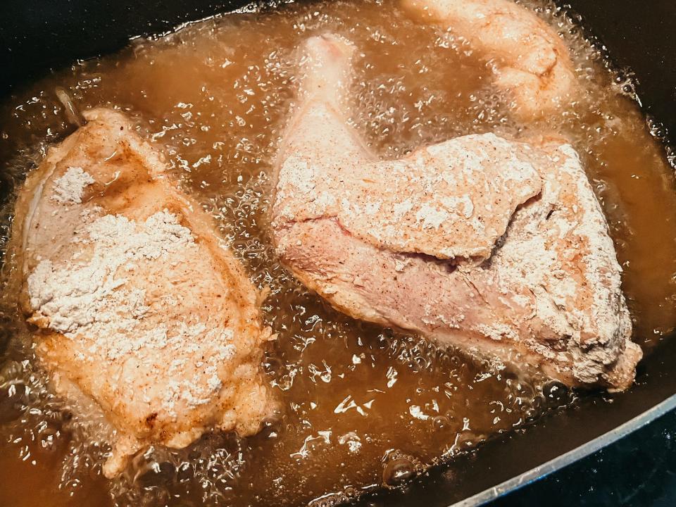 three pieces of chicken frying in a pan of hot oil